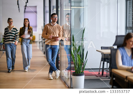 Businessman standing by glass wall in a modern office corridor, holding a digital tablet and smiling with reflection visible on the glass, symbolizing success, optimism, and modern business lifestyle. 133353737