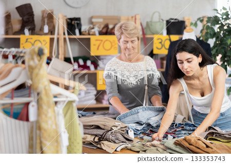 Armenian woman stands next to a mature woman near the counter in clothes store Armenian woman stands next to a mature woman near the counter in clothes store 133353743
