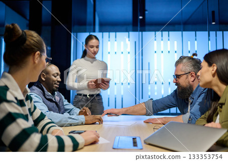 Diverse business team gathered around a table discussing analytics during a meeting in a modern office. Laptop screen shows charts and graphs, symbolizing teamwork, communication, and data driven Diverse business team gathered around a table discussing analytics during a meeting in a modern office. Laptop screen shows charts and graphs, symbolizing teamwork, communication, and data driven 133353754
