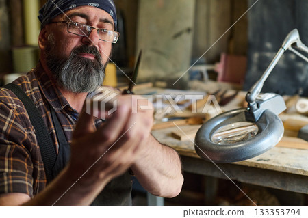 Artisan woodworker carving wood with knife in workshop, craftsman carefully shaping wood with hand tools, hobbyist creating handmade crafts, woodworking project in studio. 133353794