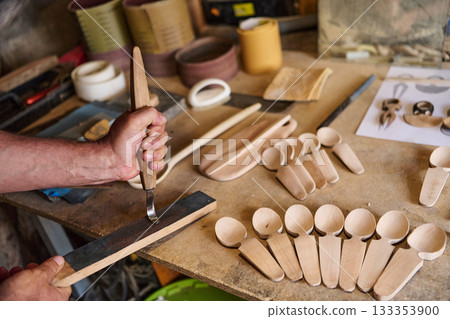 Handcrafting wooden spoons, a craftsman carving wood with a gouge, handmade wooden kitchenware, traditional wood carving tools on a workbench, artisan workshop, craft process Handcrafting wooden spoons, a craftsman carving wood with a gouge, handmade wooden kitchenware, traditional wood carving tools on a workbench, artisan workshop, craft process 133353900