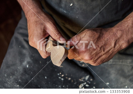 Close-up of a craftsman's hands carving wood with a sharp knife, shaping a wooden object, woodworking project, handmade craft, artisan skill, detailed handwork, artistic creation, small business 133353908