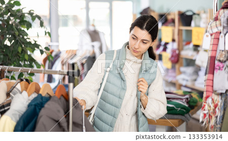 Girl chooses fashionable down jacket in clothing boutique Girl chooses fashionable down jacket in clothing boutique 133353914