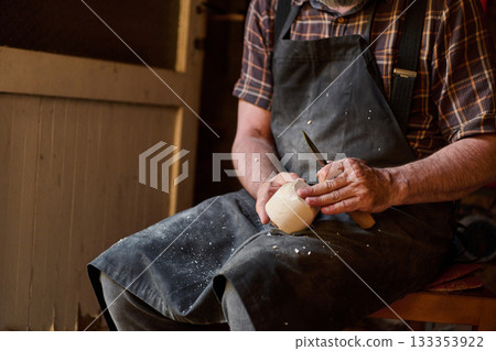 Woodcarver at work, carving a wooden object with a knife, creating a handmade piece, craftsmanship and traditional skills, woodworking artistry, indoor scene, close up detail. Woodcarver at work, carving a wooden object with a knife, creating a handmade piece, craftsmanship and traditional skills, woodworking artistry, indoor scene, close up detail. 133353922