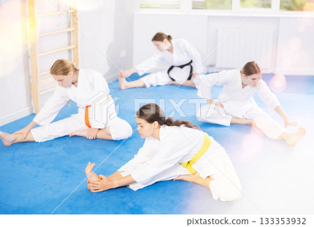 Teenage girl doing stretching exercises after intense martial arts training Teenage girl doing stretching exercises after intense martial arts training 133353932