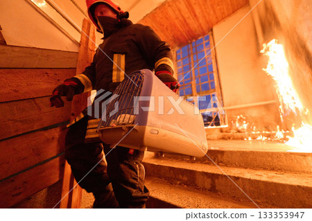 Brave firefighter carrying a rescued cat in a portable cage down smoky stairs during a building fire, symbolizing courage, compassion, and dedication to saving both human and animal lives in 133353947