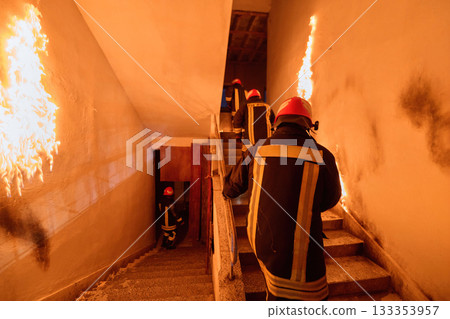 Firefighters in action, climbing stairs amidst flames and smoke, emergency response, fire safety, professional rescue team, danger and courage, indoor scene. Firefighters in action, climbing stairs amidst flames and smoke, emergency response, fire safety, professional rescue team, danger and courage, indoor scene. 133353957