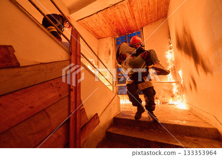 Courageous firefighter carrying a rescued woman down a burning staircase during an emergency evacuation, symbolizing bravery, heroism, and dedication to saving lives in dangerous situations. Courageous firefighter carrying a rescued woman down a burning staircase during an emergency evacuation, symbolizing bravery, heroism, and dedication to saving lives in dangerous situations. 133353964