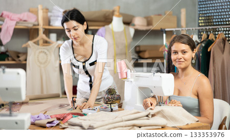 Female dressmaker cutting paper next to assistant Female dressmaker cutting paper next to assistant 133353976