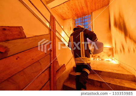 Brave firefighter carrying a rescued cat in a portable cage down smoky stairs during a building fire, symbolizing courage, compassion, and dedication to saving both human and animal lives in 133353985