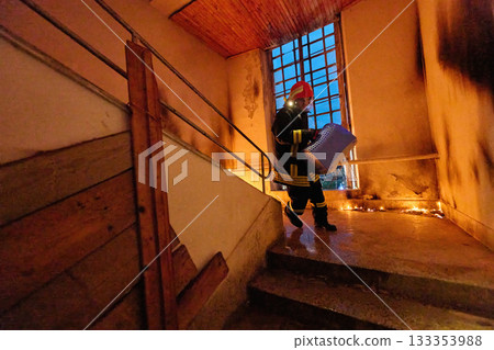 Brave firefighter carrying a rescued cat in a portable cage down smoky stairs during a building fire, symbolizing courage, compassion, and dedication to saving both human and animal lives in 133353988