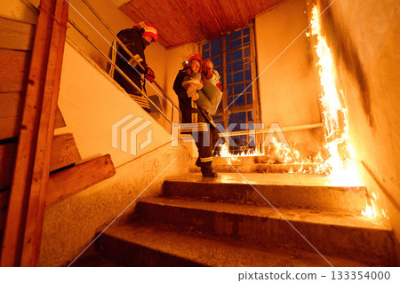 Courageous firefighter carrying a rescued woman down a burning staircase during an emergency evacuation, symbolizing bravery, heroism, and dedication to saving lives in dangerous situations. 133354000