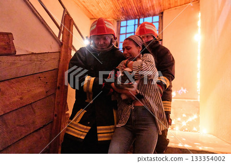 Two brave firefighters helping a frightened woman carrying her cat to safety from a burning building, symbolizing heroism, compassion, and teamwork during an emergency rescue operation. Two brave firefighters helping a frightened woman carrying her cat to safety from a burning building, symbolizing heroism, compassion, and teamwork during an emergency rescue operation. 133354002
