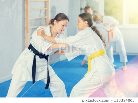 Pairs classes in judo or jiu jitsu - two teenage girls practice grabbing and throwing on sports mats 133354003