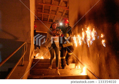 Two brave firefighters helping a frightened woman carrying her cat to safety from a burning building, symbolizing heroism, compassion, and teamwork during an emergency rescue operation. Two brave firefighters helping a frightened woman carrying her cat to safety from a burning building, symbolizing heroism, compassion, and teamwork during an emergency rescue operation. 133354010