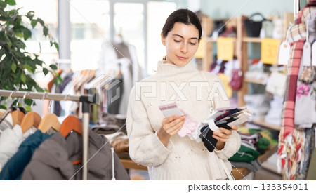 Girl chooses warm socks for winter in clothing store 133354011