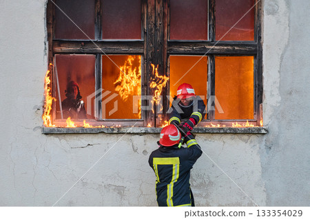 Firefighter rescuing a baby from burning building, fireman in action saving child, emergency situation, fire in house, danger, rescue operation, outdoor scene 133354029