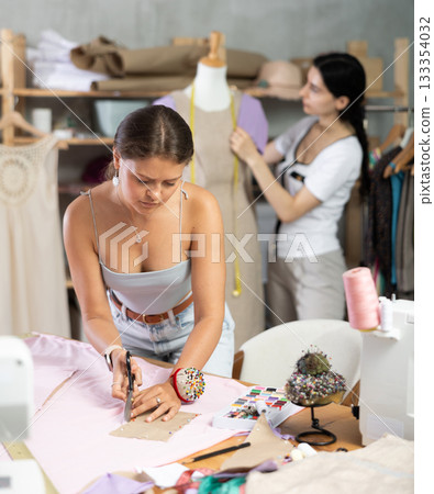Dressmaker cuts off a piece of fabric against the background of the assistant 133354032