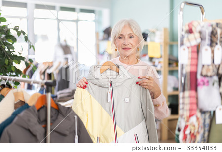 Mature woman chooses fashionable coat or jacket in clothing store Mature woman chooses fashionable coat or jacket in clothing store 133354033