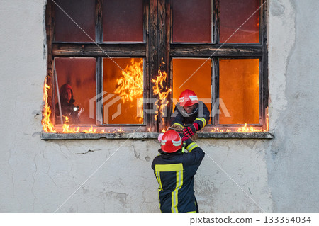 Firefighter rescuing a baby from burning building, fireman in action saving child, emergency situation, fire in house, danger, rescue operation, outdoor scene Firefighter rescuing a baby from burning building, fireman in action saving child, emergency situation, fire in house, danger, rescue operation, outdoor scene 133354034