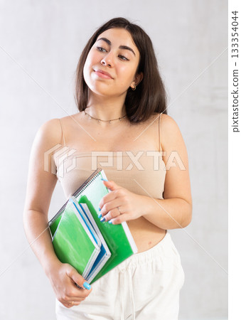 Young woman posing with notebooks against wall Young woman posing with notebooks against wall 133354044