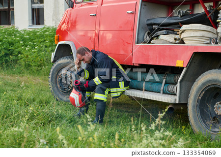 Thoughtful Firefighter in Uniform Sits on Firetruck, Contemplating Rescue Operations, Emergency Services, Fire Safety, Training, and Community Support, Surrounded by Nature 133354069