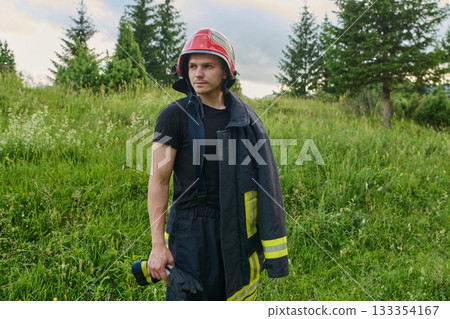 Portrait of a confident firefighter in helmet and uniform standing in a sunlit field, ready for action and emergency response, showcasing bravery and dedication. 133354167