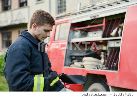 Firefighter preparing equipment near fire truck, wearing uniform, ready for emergency response, rescue operation, fire safety, service and protection, outdoor scene with building background Firefighter preparing equipment near fire truck, wearing uniform, ready for emergency response, rescue operation, fire safety, service and protection, outdoor scene with building background 133354193
