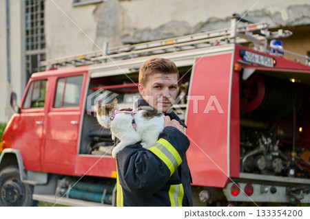 Brave firefighter holding a rescued cat in front of a fire engine, showcasing heroism and compassion, a heartwarming scene of rescue and care, outdoor setting 133354200