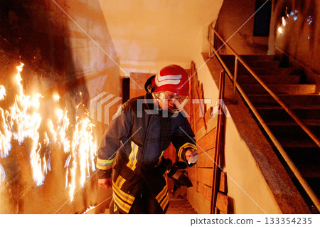 Firefighter in action, battling flames in burning building, wearing protective gear and helmet, fire safety and emergency response, danger and rescue, urban environment. 133354235