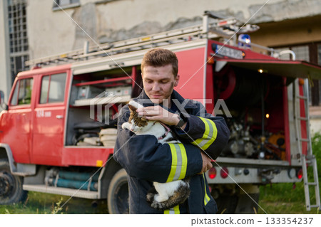 Brave firefighter holding a rescued cat in front of a fire engine, showcasing heroism and compassion, a heartwarming scene of rescue and care, outdoor setting 133354237