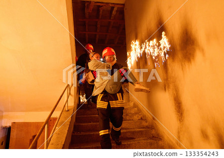 Courageous firefighter carrying a rescued woman down a burning staircase during an emergency evacuation, symbolizing bravery, heroism, and dedication to saving lives in dangerous situations. 133354243