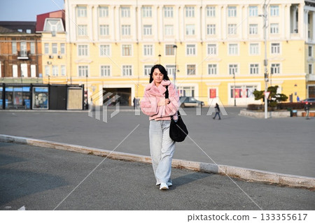 Mature 50 years old Russian woman walking outdoors in Vladivostok on an autumn day, wearing a pink jacket and jeans in an urban city setting. 133355617
