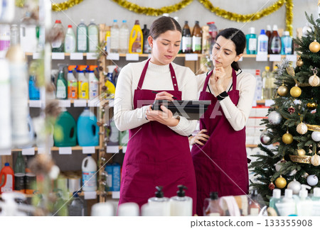 Two female sellers rewrites availability of goods in window and fills out statement on tablet Two female sellers rewrites availability of goods in window and fills out statement on tablet 133355908