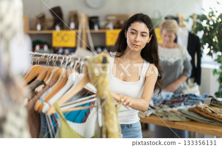 Woman choosing ribbon clothes against the background of a customer in a store Woman choosing ribbon clothes against the background of a customer in a store 133356131