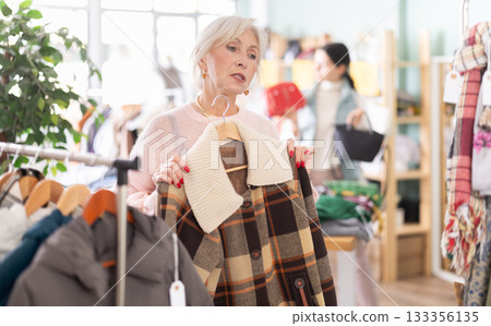 Elderly woman choosing a jacket and coat in a clothing store 133356135