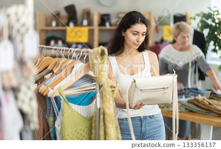 Female customer elect leather handbag in store. Female client choosing something in background Female customer elect leather handbag in store. Female client choosing something in background 133356137
