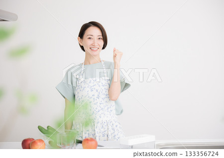 一位面帶笑容、身穿圍裙的家庭主婦在廚房準備蔬菜菜餚，並興奮地揮拳慶祝。居家飲食與健康 133356724