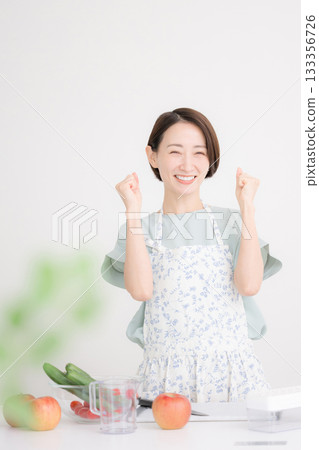 A smiling housewife in an apron prepares vegetable dishes in the kitchen and makes a fist pump. Home diet and health 133356726