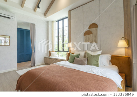 Big bedroom in cottage style with brown and green pillow. Wall lamp and wall art on wall. 133356949