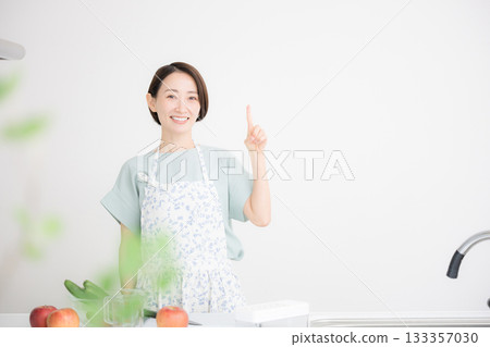 A bright kitchen scene in which a housewife in an apron smiles and points out the recommended spots for home cooking A bright kitchen scene in which a housewife in an apron smiles and points out the recommended spots for home cooking 133357030