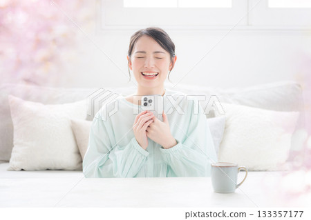 A cute and happy indoor lifestyle of a Japanese woman holding her smartphone to her chest and smiling. I'm so happy! 133357177