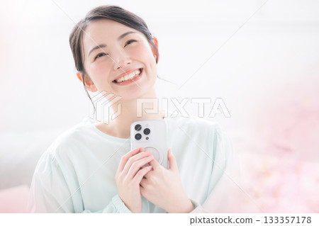 A cute and happy indoor lifestyle of a Japanese woman holding her smartphone to her chest and smiling. I'm so happy! A cute and happy indoor lifestyle of a Japanese woman holding her smartphone to her chest and smiling. I'm so happy! 133357178