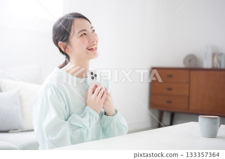 Cute happy Japanese woman holding smartphone to her chest and smiling indoor lifestyle 133357364