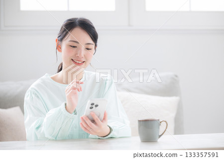 A cute Japanese woman holding a smartphone and smiling, feeling happy indoors. Image of frequently asked questions for inquiries. A cute Japanese woman holding a smartphone and smiling, feeling happy indoors. Image of frequently asked questions for inquiries. 133357591