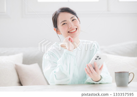 一位可愛的日本女性手持智慧型手機，面帶微笑，在室內顯得十分快樂。諮詢和常見問題。 133357595