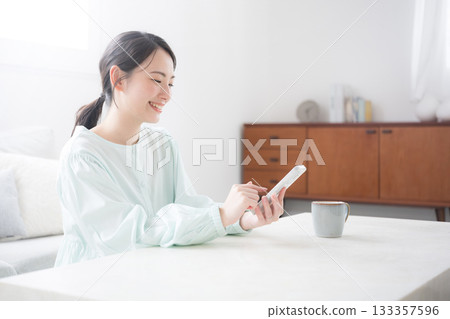 一位可愛的日本女性手持智慧型手機,面帶微笑,在室內顯得十分快樂。諮詢和常見問題。 一位可愛的日本女性手持智慧型手機,面帶微笑,在室內顯得十分快樂。諮詢和常見問題。 133357596