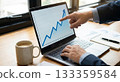 一位商人的手指向筆記型電腦螢幕上顯示的上升圖表。 133359584