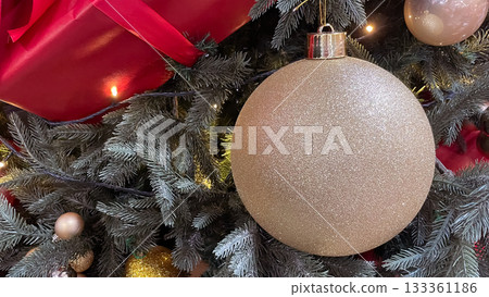Large glittering gold Christmas bauble with a gift and pine needles background. Copy space. Large glittering gold Christmas bauble with a gift and pine needles background. Copy space. 133361186