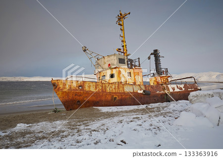 A ship abandoned out by the sea on a sandy beach against a blue sky. Winter landscape A ship abandoned out by the sea on a sandy beach against a blue sky. Winter landscape 133363916